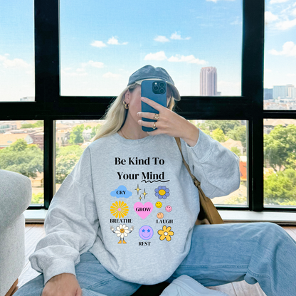 Person wearing a sweatshirt with motivational text and emojis, sitting by a window with a cityscape view.