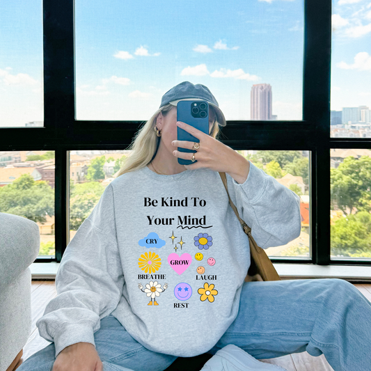 Person wearing a sweatshirt with motivational text and emojis, sitting by a window with a cityscape view.